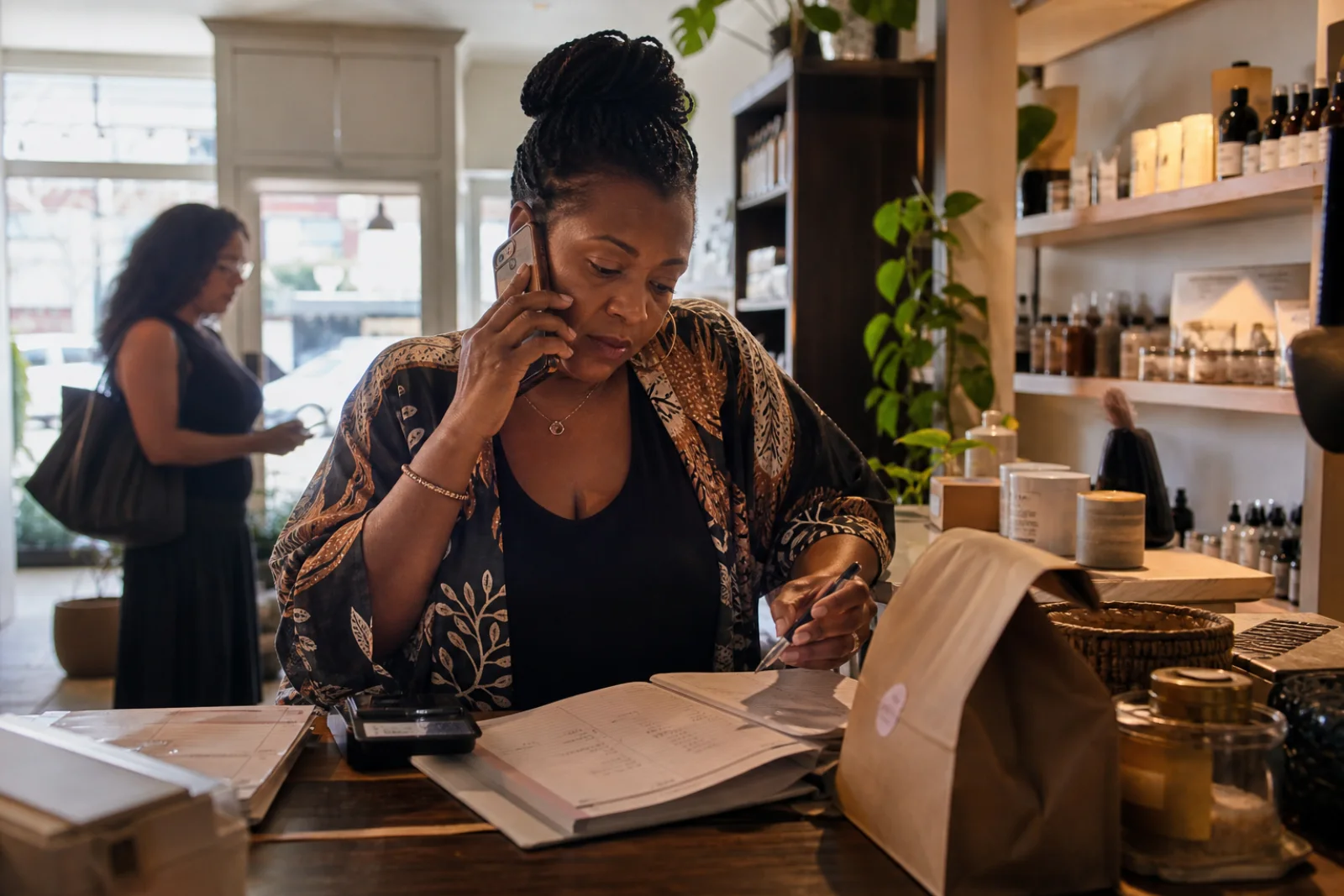 A neighborhood shop owner handling a customer call and her appointment book at the counter